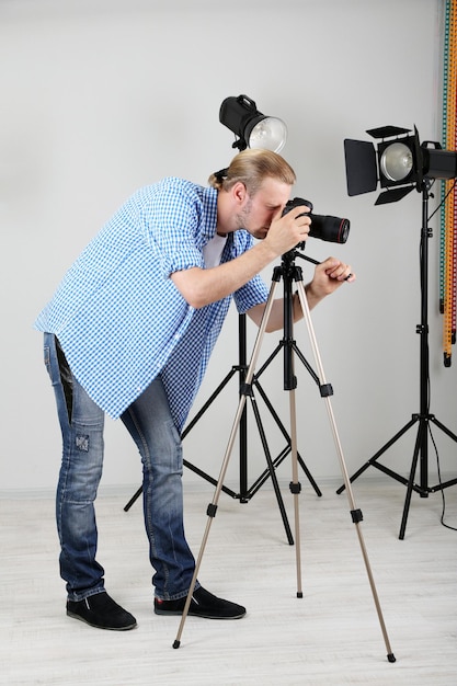 Fotografo bello con la macchina fotografica al lavoro sullo sfondo dello studio fotografico