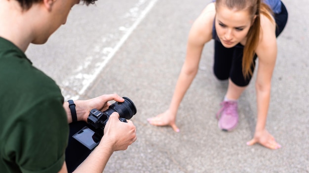 Fotografo che cattura il colpo di una giovane donna bionda in abiti sportivi che si prepara per iniziare a correre in allenamento all'aperto, su strada