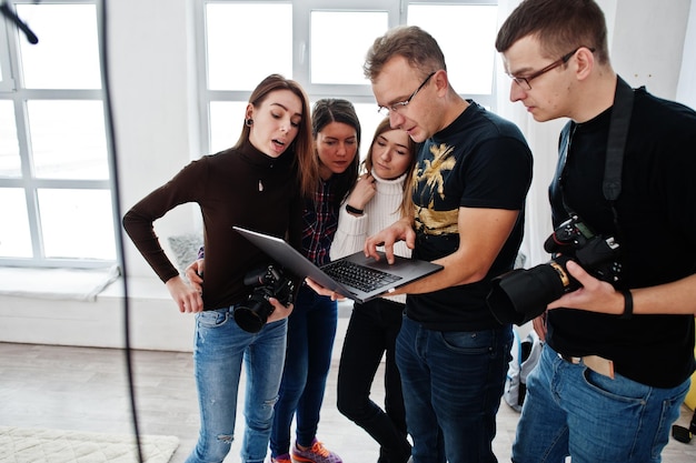 Fotografo che spiega lo scatto al suo team in studio e guarda sul laptop Parla con i suoi assistenti in possesso di una macchina fotografica durante un servizio fotografico Lavoro di squadra e brainstorming