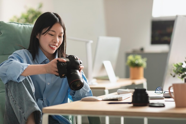 Fotografo cinese signora che lavora tenendo la fotocamera seduta in studio fotografico