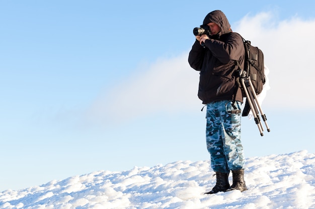 Fotografo del giovane nell'abbigliamento di inverno che sta e che fa foto al sole