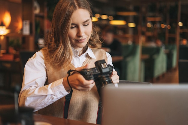 Fotografo di giovane donna che lavora con la sua macchina fotografica con il computer portatile in un caffè