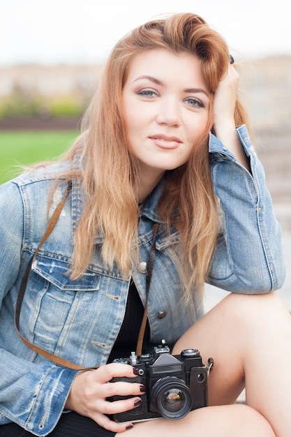 Fotografo di giovane ragazza che cammina lungo la strada in una giacca di jeans con una vecchia macchina fotografica