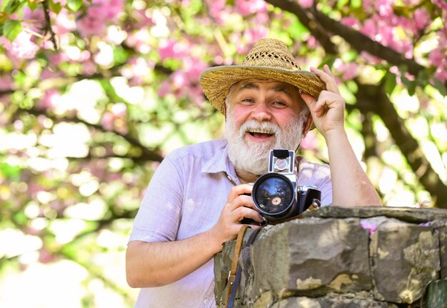 Fotografo di relax estivo uomo scatta foto di fiori di sakura Fotografo di giardini in fiore di ciliegio che scatta foto di fiori di albicocca stagione primaverile con fiore rosa vecchio guarda piante giovani