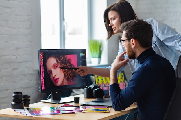 Fotografo e graphic designer che lavorano in ufficio con laptop, monitor, tavoletta grafica e tavolozza di colori.