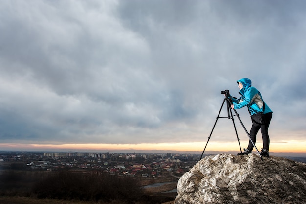 Fotografo femminile con la macchina fotografica sul treppiede sulla grande roccia