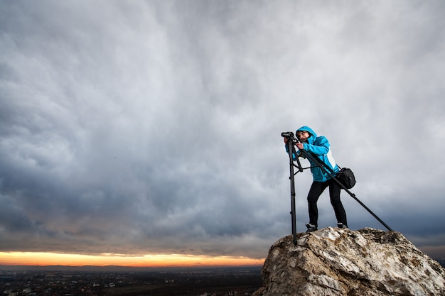 Fotografo femminile con la macchina fotografica sul treppiede sulla grande roccia