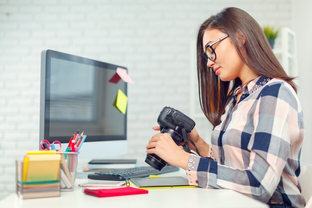 Fotografo grazioso della giovane donna con la macchina fotografica in ufficio