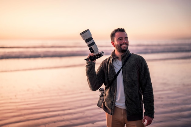 Fotografo latino in possesso di fotocamera professionale sulla spiaggia e ritratto sorridente