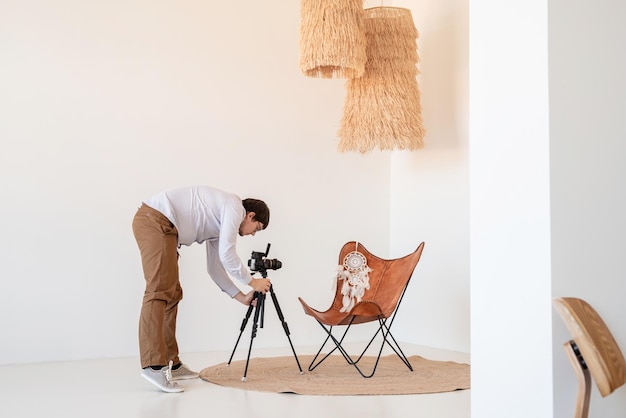 Fotografo maschio che lavora in interni luminosi e ariosi minimi, sedia, tappeto e cuscini bianchi e beige