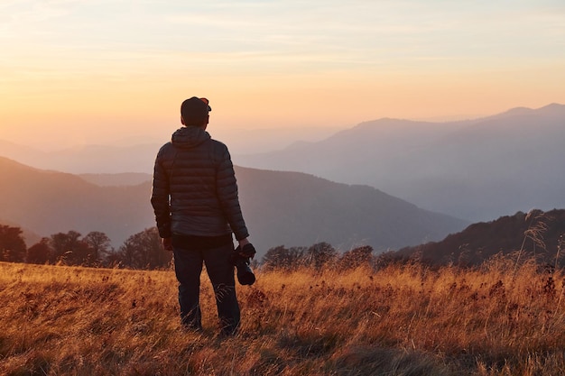 Fotografo maschio in piedi e che lavora al maestoso paesaggio di alberi autunnali e montagne all'orizzonte