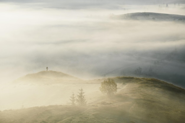 Fotografo paesaggista con un treppiede in montagna Nebbia mattutina autunnale Veduta dall'alto dalla collina