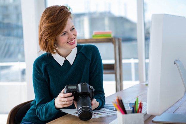 fotografo sorridente hipster, seduto alla sua scrivania, guardando la sua macchina fotografica