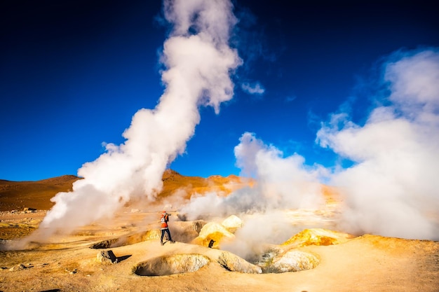 Fotografo tra l'enorme area di geyser fumanti del sole in Bolivia