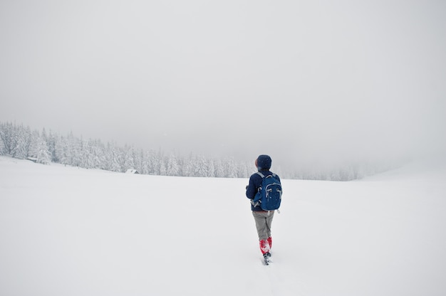 Fotografo turistico dell'uomo con lo zaino, alla montagna con i pini coperti da neve