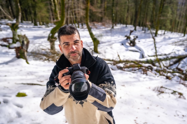 Fotografo uomo che scatta una foto sulla neve godendosi la fotografia invernale in un bosco innevato