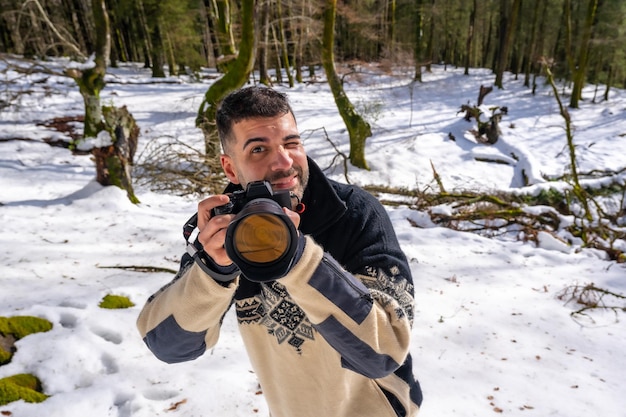 Fotografo uomo che scatta una foto sulla neve godendosi la fotografia invernale in una foresta di faggio