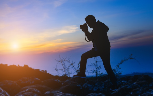 fotografo uomo con una macchina fotografica sulla cima della montagna con il cielo al tramonto