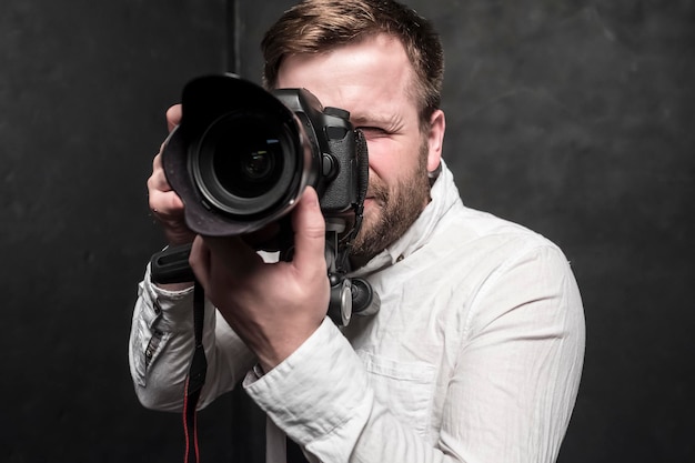 fotografo uomo grazioso in camicia bianca spara in studio su una fotocamera DSLR che si trova su treppiede