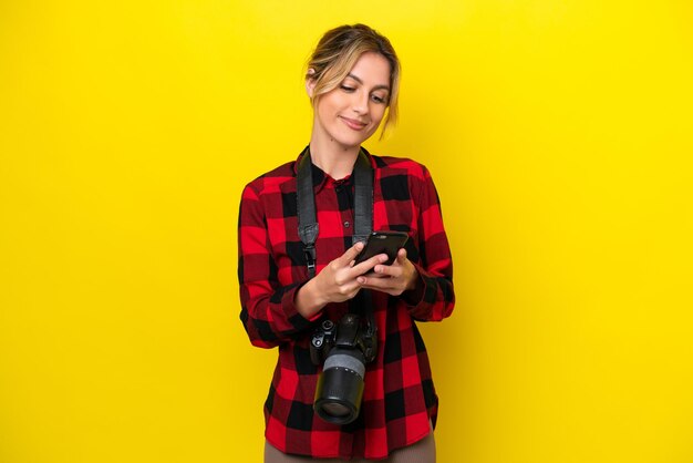 Fotografo uruguaiano donna isolata su sfondo giallo che invia un messaggio con il cellulare