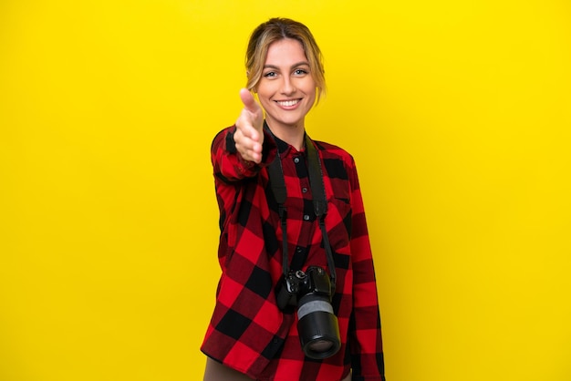 Fotografo uruguaiano donna isolata su sfondo giallo che stringe le mani per chiudere un buon affare
