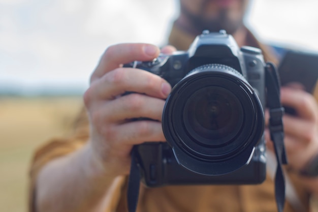 Fotografo viaggiatore con una macchina fotografica in mano sullo sfondo di un campo e mucchi di fieno.