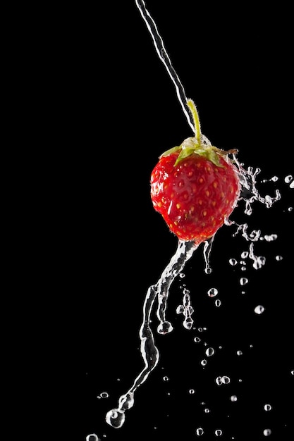 Fragola, bacca con gocce d'acqua che cadono su uno sfondo scuro