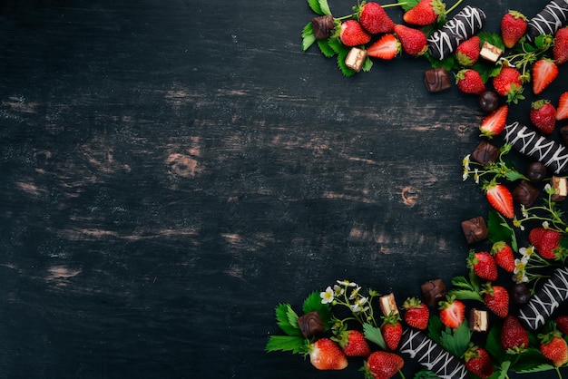 Fragola con cioccolato e caramelle su uno sfondo di legno nero Vista dall'alto Spazio di copia