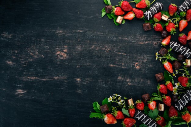 Fragola con cioccolato e caramelle su uno sfondo di legno nero Vista dall'alto Spazio di copia