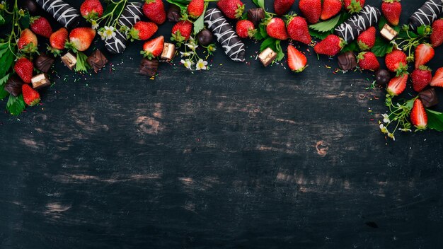 Fragola con cioccolato e caramelle su uno sfondo di legno nero Vista dall'alto Spazio di copia