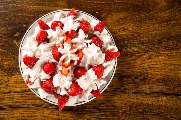 Fragola con crema chantilly in un piatto su un tavolo di legno