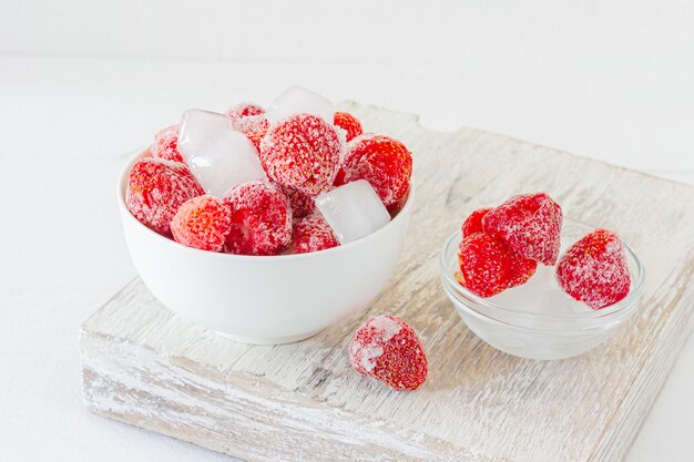 Fragola congelata con cristalli di ghiaccio su sfondo bianco.