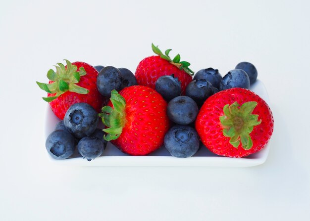 Fragola e mirtillo freschi e dolci su fondo bianco, frutta sana e dieta.