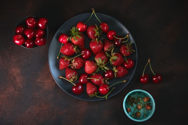 Fragola organica fresca e ciliegia dolce in lastra di pietra su superficie strutturata scura