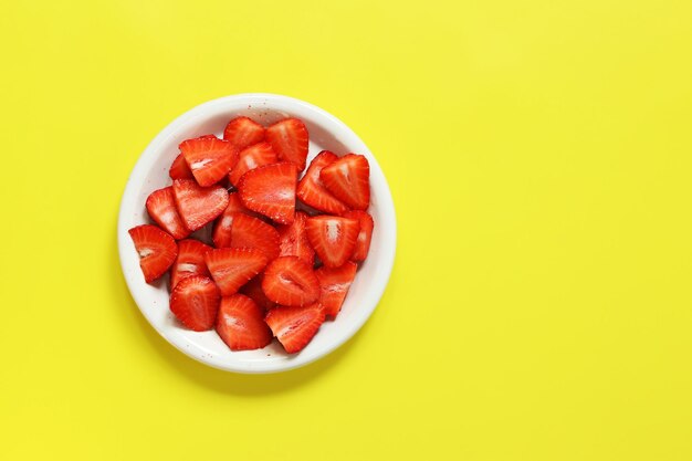 Fragole a fette in un piatto su sfondo giallo vista dall'alto piatto lay Fragole fresche