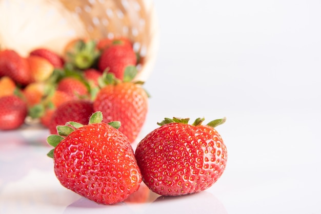 Fragole, bellissime fragole cadute da un cesto intrecciato di paglia su una superficie bianca, messa a fuoco selettiva.