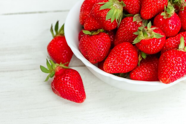 Fragole deliziose mature fresche in una ciotola bianca su superficie di legno