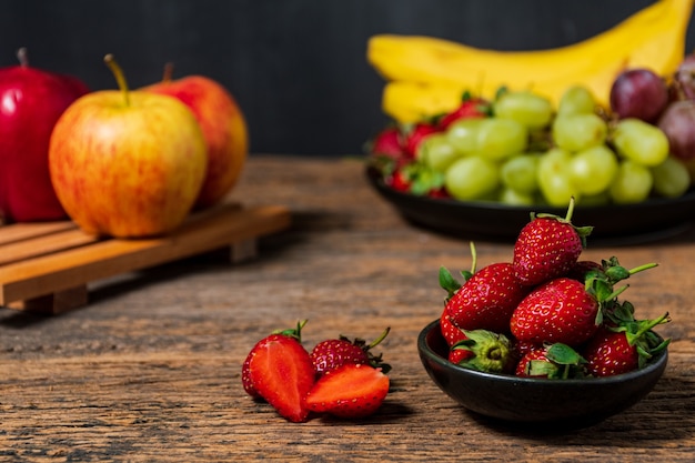 Fragole di vista laterale con mele e uva in un cesto sulla parete di fondo in legno Foto Gratuite