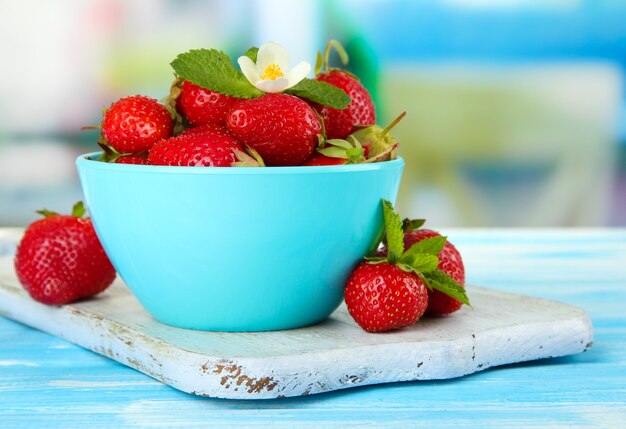 Fragole dolci mature in ciotola sulla tavola di legno blu