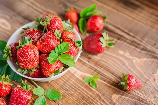 Fragole dolci mature in piatto bianco sui precedenti di legno. Copia spazio