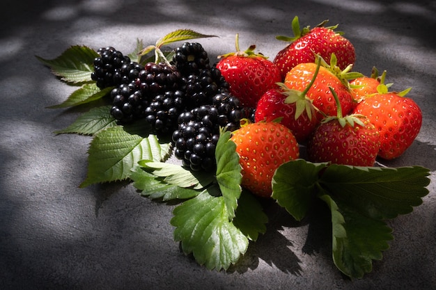 Fragole e more di natura morta su sfondo scuro alla luce naturale del sole