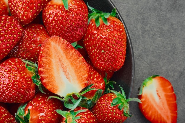 Fragole estive appena raccolte bacca tagliata a metà e bacche intere Fragole mature in una ciotola scura vista dall'alto Sfondo di fragole mature delizioso dessert naturale