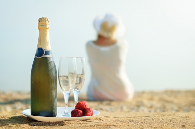 Fragole fresche di bacche, bottiglia di champagne, bicchieri e la donna sulla spiaggia.