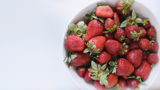 Fragole fresche e deliziose in una ciotola bianca isolata su uno sfondo bianco, vista dall'alto