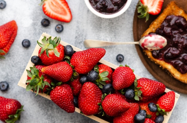 Fragole fresche e mirtilli una fetta di pane tostato con marmellata e marmellata in una ciotola bianca