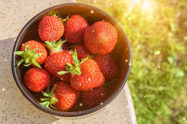 Fragole fresche, illuminate dalla luce del sole, in un piatto nero su un tavolo di granito.