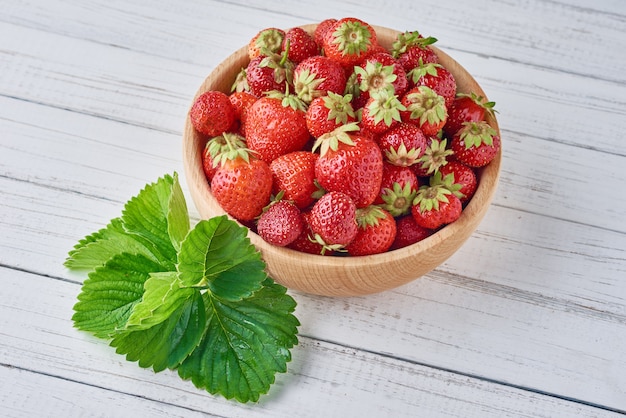 Fragole fresche in ciotola e foglie verdi di legno su fondo grigio, fine su