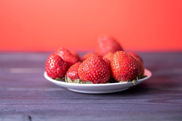 Fragole fresche in un piatto bianco su uno sfondo di legno scuro