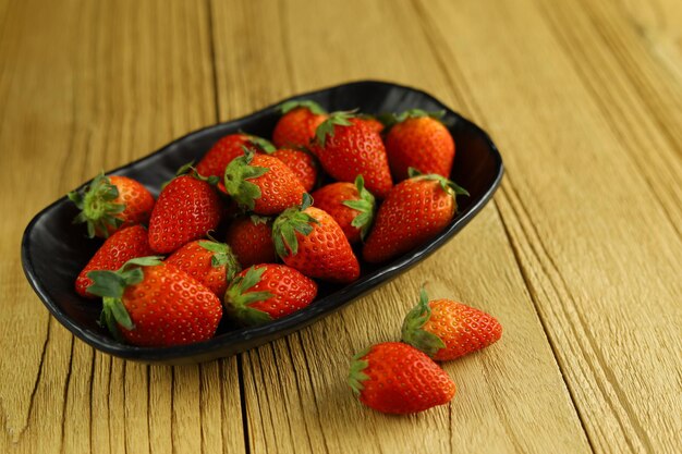 Fragole fresche in una banda nera sulle fragole di legno in una ciotola di legno sulla tavola di legno