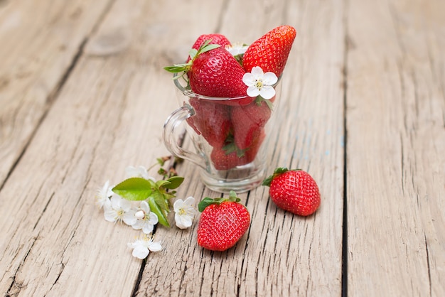 Fragole fresche in una tazza di vetro su una tavola di legno